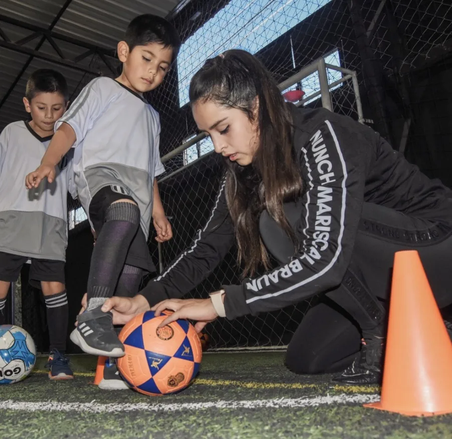 Entrenadora guiando a un niño con el balón en Baby Braun