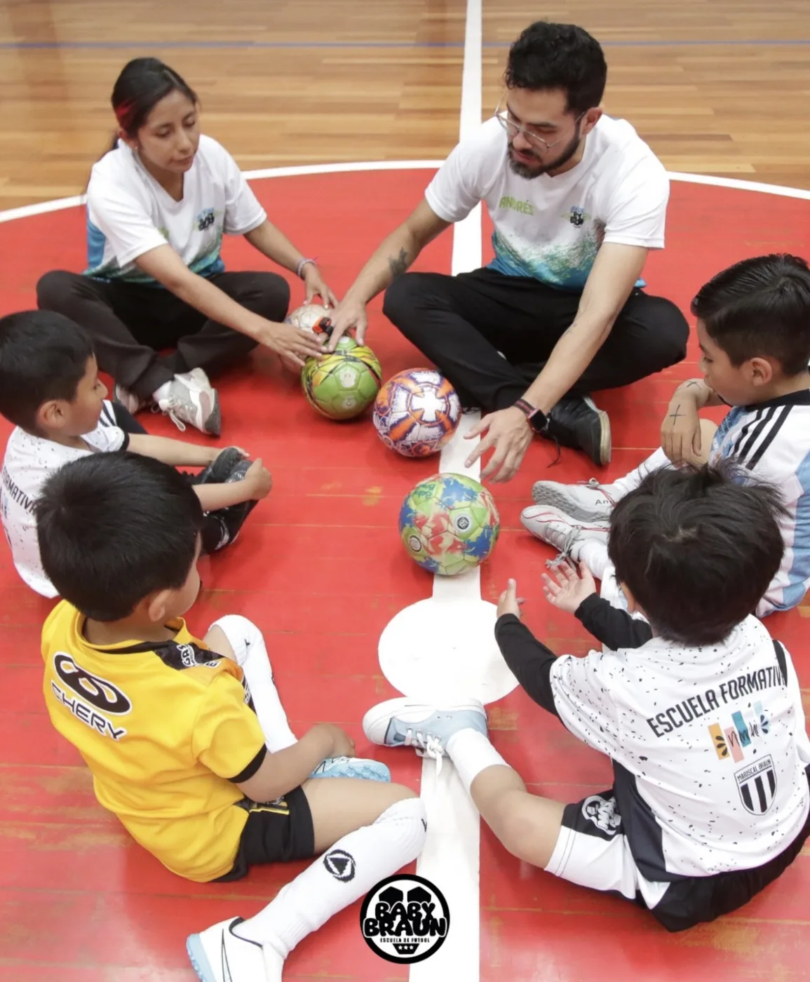 Niños y entrenadores sentados en círculo con balones en Baby Braun